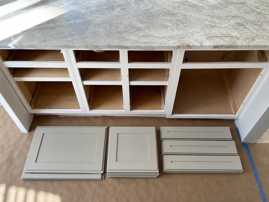 Base cabinet boxes with their doors removed, and new painted shaker doors and drawer fronts stacked in front of them